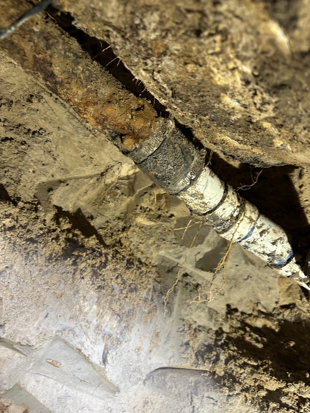 Old cast iron drain line exposed in a tunnel under a house
